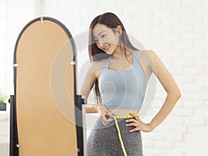 Happy girl measuring waist with tape  in front of mirror. Weight Loss