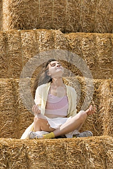 Happy girl meditating or relaxing in nature. Young woman on sitting lotus yoga pose on hay background