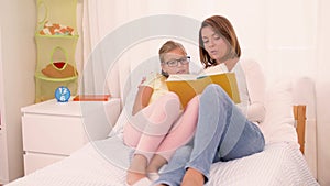 Happy girl with mother reading book at home
