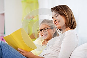 Happy girl with mother reading book at home