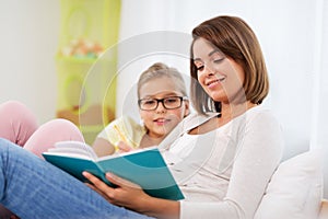Happy girl with mother reading book at home