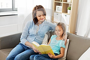 Happy girl with mother reading book at home