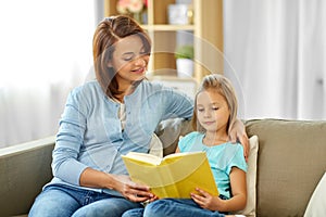 Happy girl with mother reading book at home