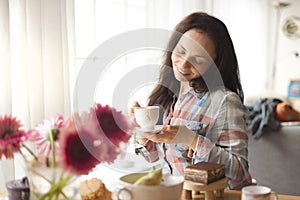 Happy girl with a mug of fragrant coffee in hands. Good breakfast at home in the living room by the window. Free space for text.