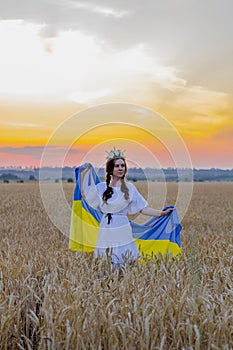 Happy girl in national Ukrainian embroidered shirt with wreath on his head hold large yellow-blue flag against background