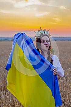 Happy girl in national Ukrainian embroidered shirt with wreath on his head hold large yellow-blue flag against background