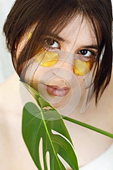 Happy girl with natural skin and lifting anti-wrinkle collagen patches under eyes and green palm leaf. Portrait of beautiful young