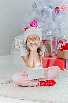 Happy girl opens a magical glowing Christmas gift while sitting near Christmas tree