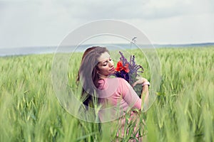 Happy girl outdoors on green wheat field in summer nature holding bunch bouquet of poppy and lavender flowers. Pretty woman with