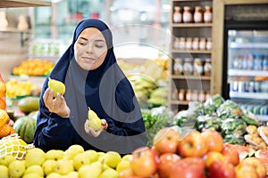 Happy girl in paranja making purchases in supermarket, choosing fresh ripe pears