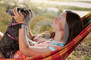 Happy girl on a picnic lying in a hammock holding a small dog in her arms, lifestyle
