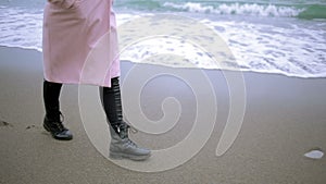 Happy girl in pink coat near the sea during a storm. Sea washes its footprints in the sand
