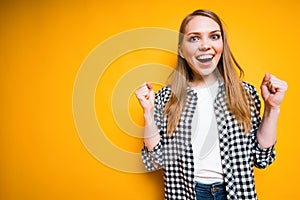 Happy girl in a plaid shirt rejoices in victory clenching her hands into fists, opening her mouth photo