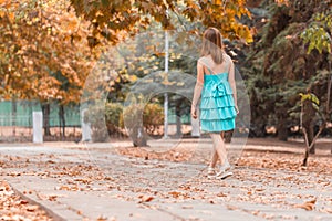 Happy girl playfully walks along autumn street in good mood. Dancing young woman in turquoise dress with beautiful legs. Freedom