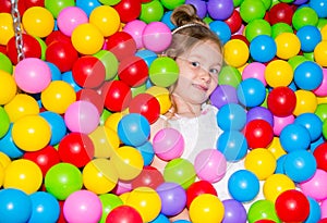 Happy girl playing in ball pit on birthday party in kids amusement park and indoor play center. Child playing with