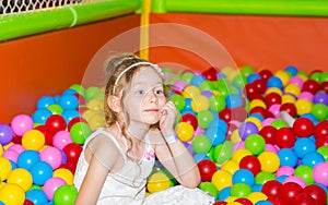 Happy girl playing in ball pit on birthday party in kids amusement park and indoor play center. Child playing with colorful balls