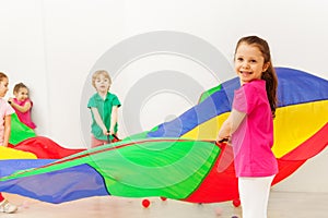 Happy girl playing with colorful parachute in gym