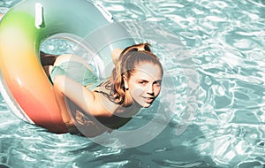 Happy girl playing with colorful swim ring in swimming pool. Young woman play in tropical resort. Family beach vacation