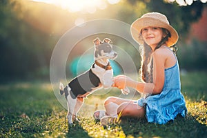 Happy girl playing with cute playful puppy little dog outdoor on a sunny day in a park