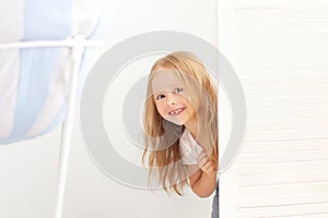 Happy girl playing hide and seek in wardrobe. Active child looking hiding behind a white door. A child with a happy face, playing