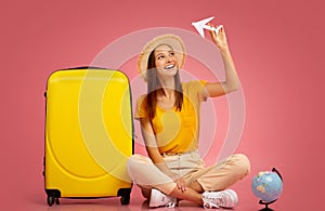 Happy girl playing with paper airplane, sitting next to suitcase