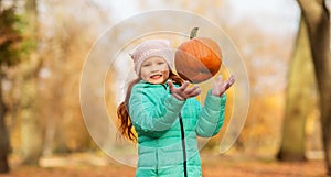 Happy girl playing with pumpkin at autumn park