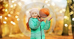 Happy girl playing with pumpkin at autumn park