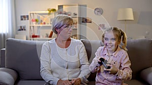 Happy girl playing video game, upset granny enviously looking at granddaughter