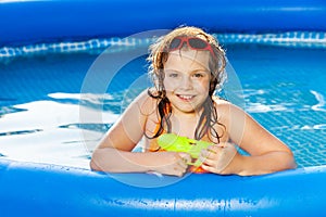 Happy girl playing with water gun in the pool