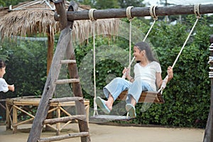 Happy girl playing on the wooden swing in the playground