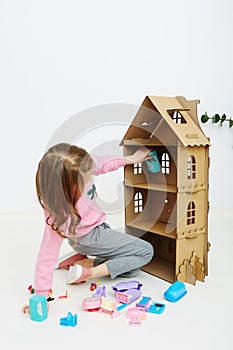 Happy girl plays with doll house and doll house furniture. Funny lovely child is having fun.