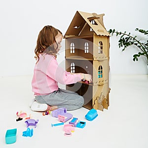 Happy girl plays with doll house and doll house furniture. Funny lovely child is having fun.