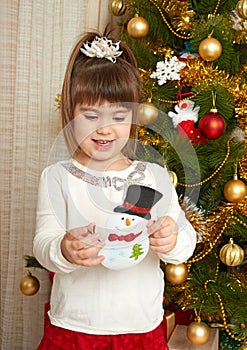 Happy girl portrait in christmas decoration, playing with snowman toy, winter holiday concept, decorated fir tree and gifts