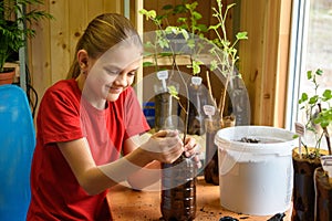 Happy girl pours soil into plastic bottles cut off under a pot for garden plants