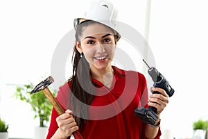 Happy girl protective helmet holds drill and hammer