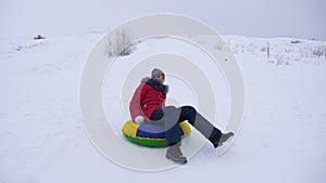 Happy girl quickly rides from high snowy mountain to snow saucer and laughs. Children`s entertainment in nature
