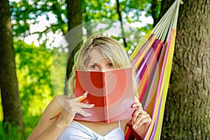 Happy girl reading a book in a hammock outdoors in the park
