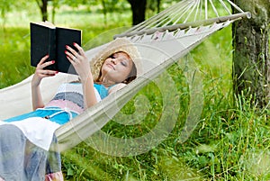 Happy girl reading in hammock in green park outdoors