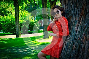 Happy girl in red dress leaning park tree in summer