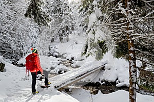 A happy girl, with a red jacket and a red backpack, crossing a wooden bridge, during a winter hiking trip