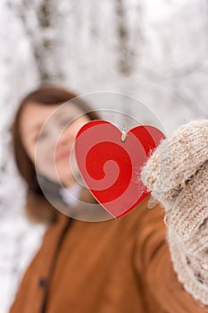 Happy girl with red wooden heart holding in hands in winter forest unfocused background. Valentines day and Christmas holidays.