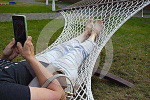 Happy girl relax on big rope hammock. Woman enjoying lie on hammock at sunny day. Female tourist in purple shirt rest