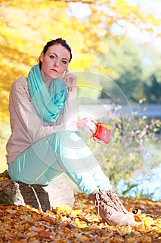 Happy girl relaxing in the autumn park enjoying hot drink
