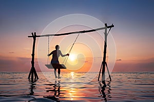 Happy girl relaxing at the beach on rope swing above sea water at sunset, summer vacation holidays resort