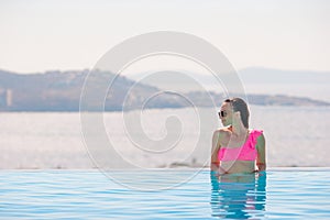 Happy girl relaxing on the edge of pool with amazing view on Mykonos, Greece