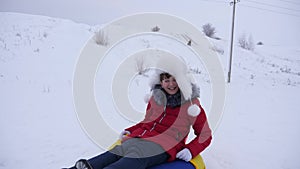 Happy girl rides with snow saucer and laughs. Child sledding in winter and smiling. Mountain resort. Christmas Holidays