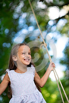 Happy girl rides on a swing in park. Little Princess has fun outdoor, summer nature outdoor. Childhood, child lifestyle, enjoyment