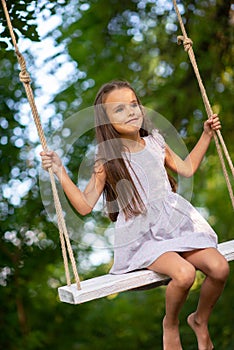 Happy girl rides on a swing in park. Little Princess has fun outdoor, summer nature outdoor. Childhood, child lifestyle, enjoyment