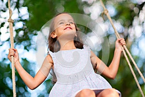 Happy girl rides on a swing in park. Little Princess has fun outdoor, summer nature outdoor. Childhood, child lifestyle, enjoyment