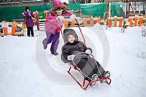 Happy girl rolling a little boy on a sled in front